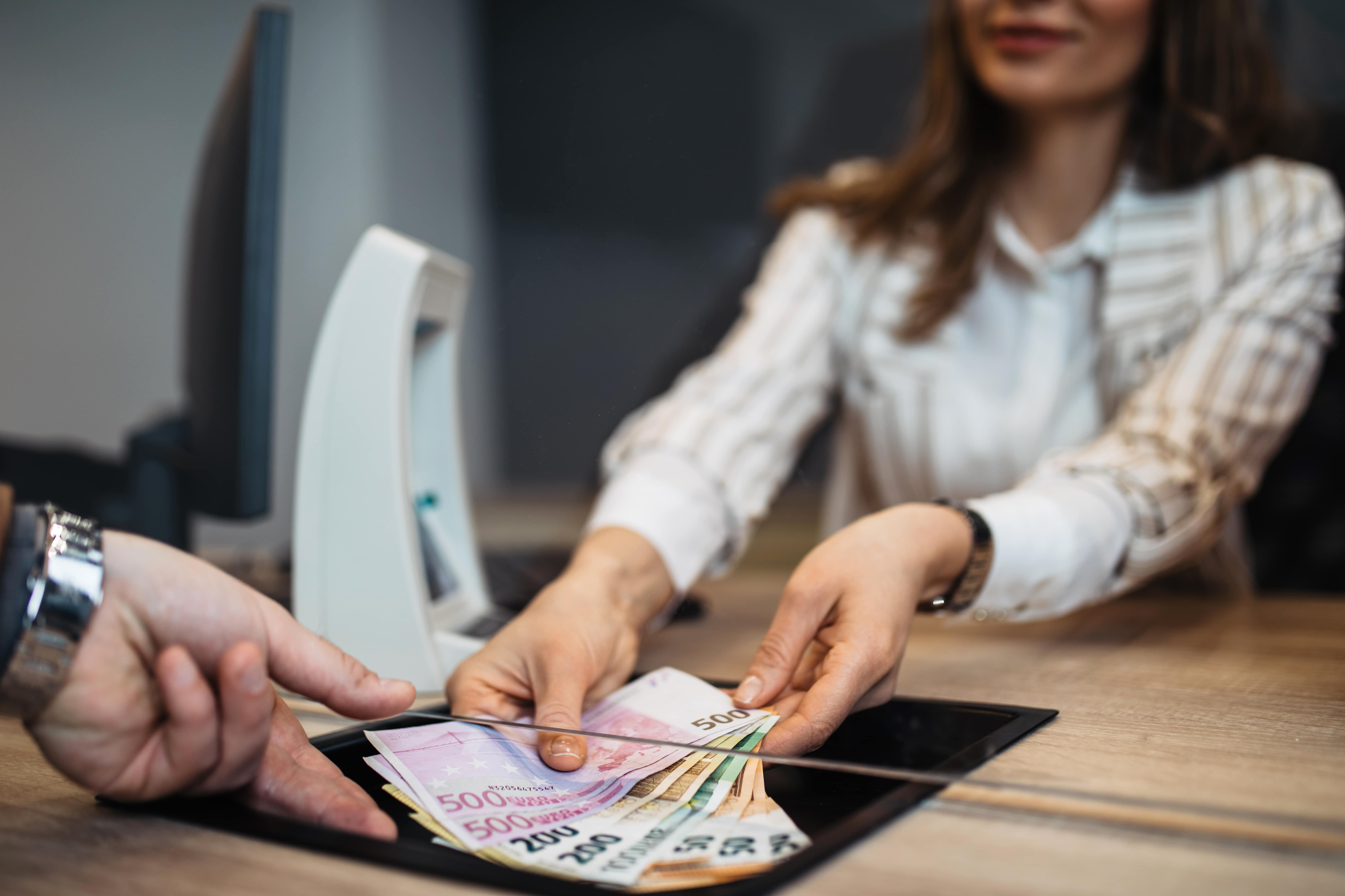 Businesswoman is working in exchange office. She is giving cash money to male customer